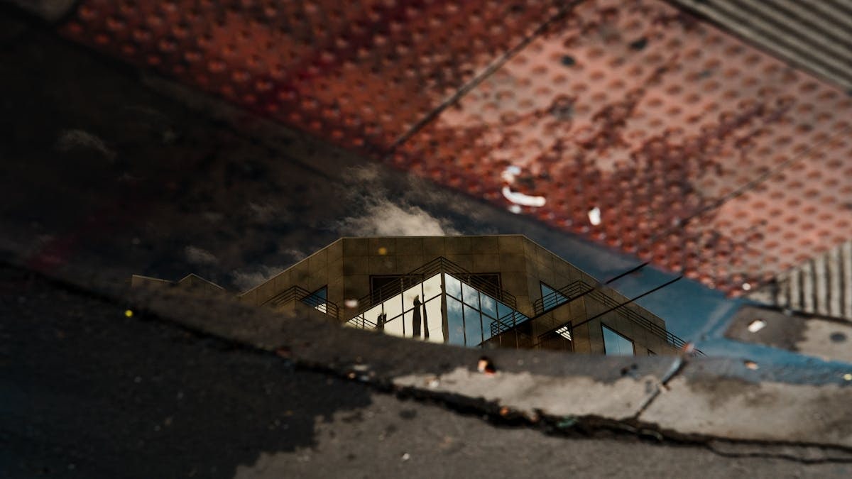 Reflection of a modern architectural building in a sidewalk puddle with textured surfaces.